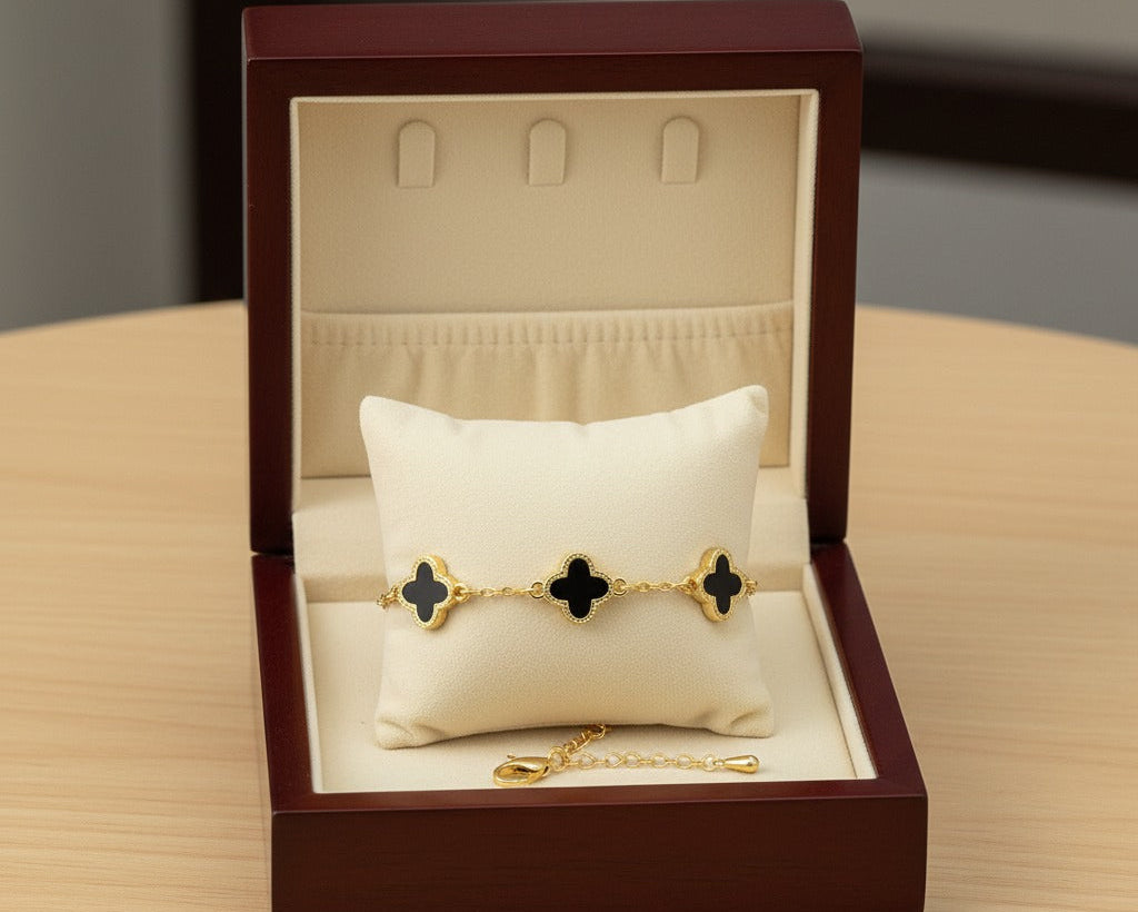 Gold bracelet with black clover designs in a jewelry box on a wooden surface