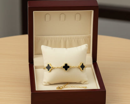 Gold bracelet with black clover designs in a jewelry box on a wooden surface