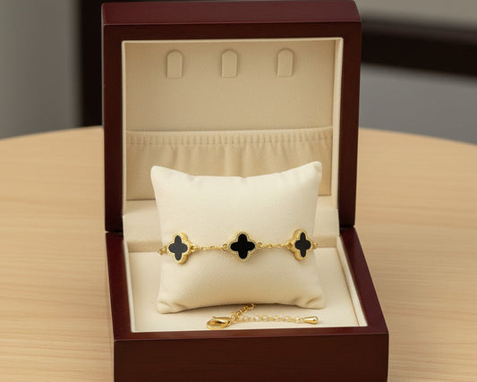 Gold bracelet with black clover designs in a jewelry box on a wooden surface
