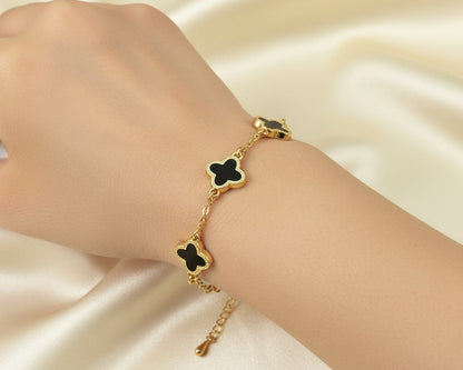 Gold bracelet with black clover-shaped charms on a hand against a satin background