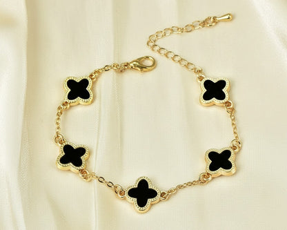 Gold bracelet with black clover-shaped charms on a beige fabric background