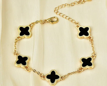Gold bracelet with black clover-shaped charms on a beige background