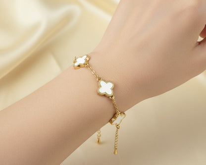 Gold bracelet with white clover-shaped charms on a beige fabric background