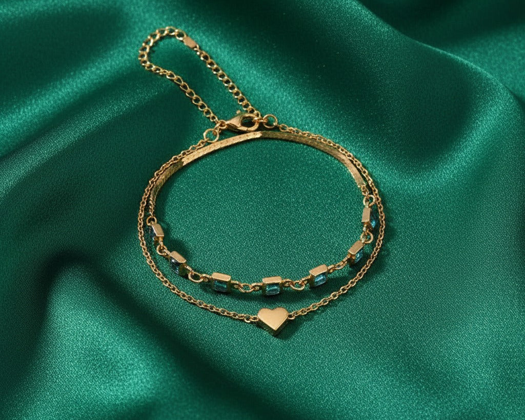 Gold bracelet with heart charm on a green satin background
