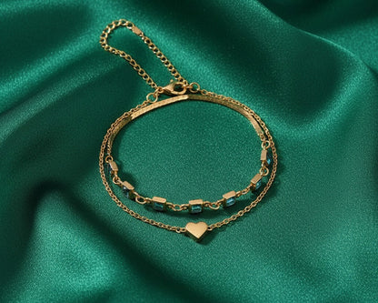 Gold bracelet with heart charm on a green satin background