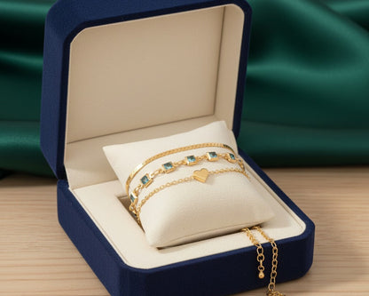 Set of gold bracelets with heart charm in a blue jewelry box on a wooden surface.