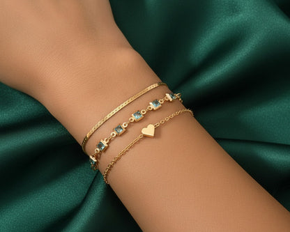 Gold bracelets with heart and star designs on a wrist against a green satin background
