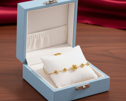 Gold bracelet on a white pillow inside an open blue jewelry box with a red fabric background