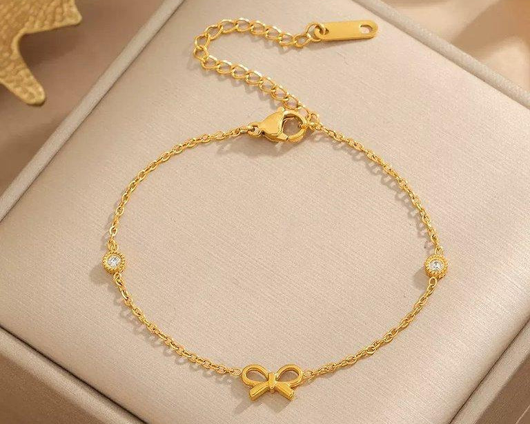Gold bracelet with a bow charm on a beige box