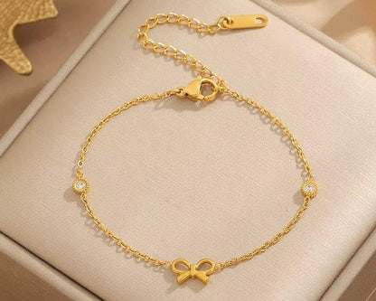 Gold bracelet with a bow charm on a beige box