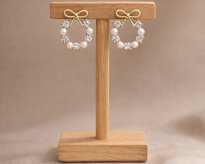 Pair of pearl wreath earrings on a wooden stand against a beige background