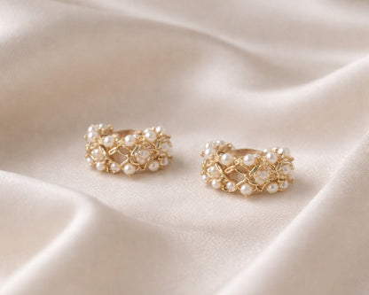 Gold earrings with pearl-like stones on a beige fabric background