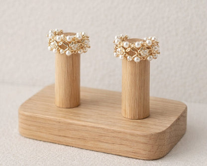 Two gold and pearl earrings on a wooden stand against a neutral background