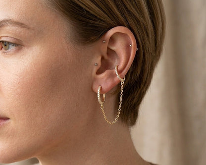 Close-up of a person wearing gold hoop earrings with a neutral background