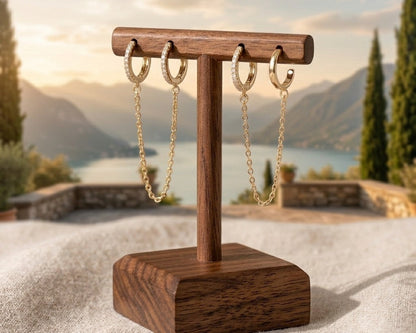 Wooden jewelry stand with gold chain earrings against a scenic background