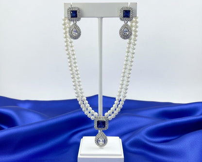 Pearl necklace with blue and silver accents on a white stand against a blue fabric background