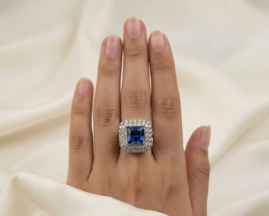 Hand wearing a ring with a blue gemstone on a beige fabric background