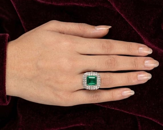 Hand wearing a ring with a green gemstone on a red velvet background
