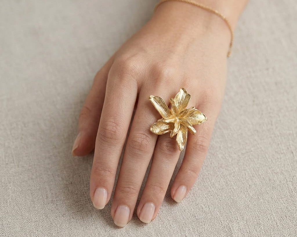 Hand wearing a gold floral ring on a neutral background