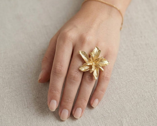 Hand wearing a gold floral ring on a neutral background