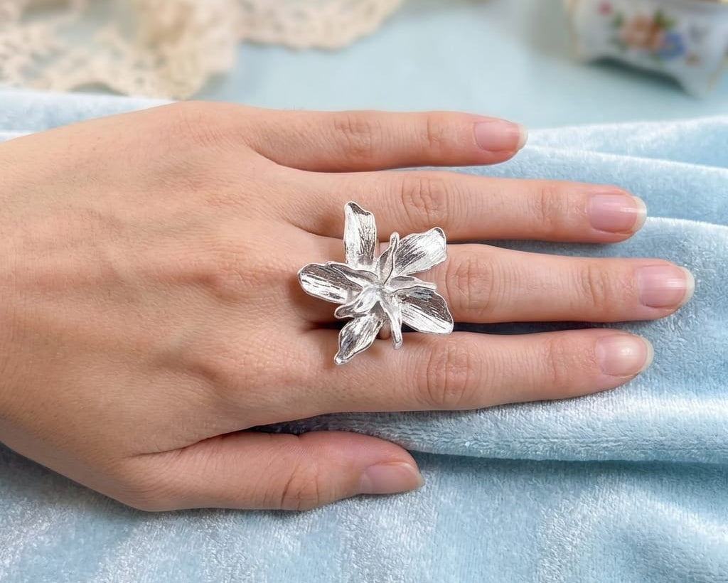 Silver flower ring on a hand with a light blue fabric background