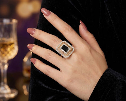 Hand wearing a diamond ring with a blurred background of a glass and dark fabric.