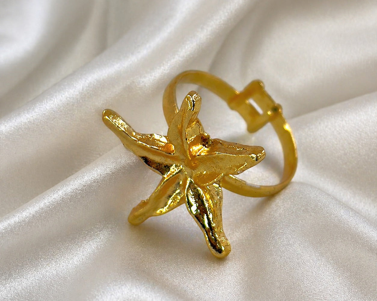 Gold starfish-shaped ring on a white fabric background
