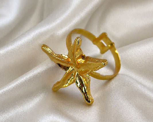 Gold starfish-shaped ring on a white fabric background