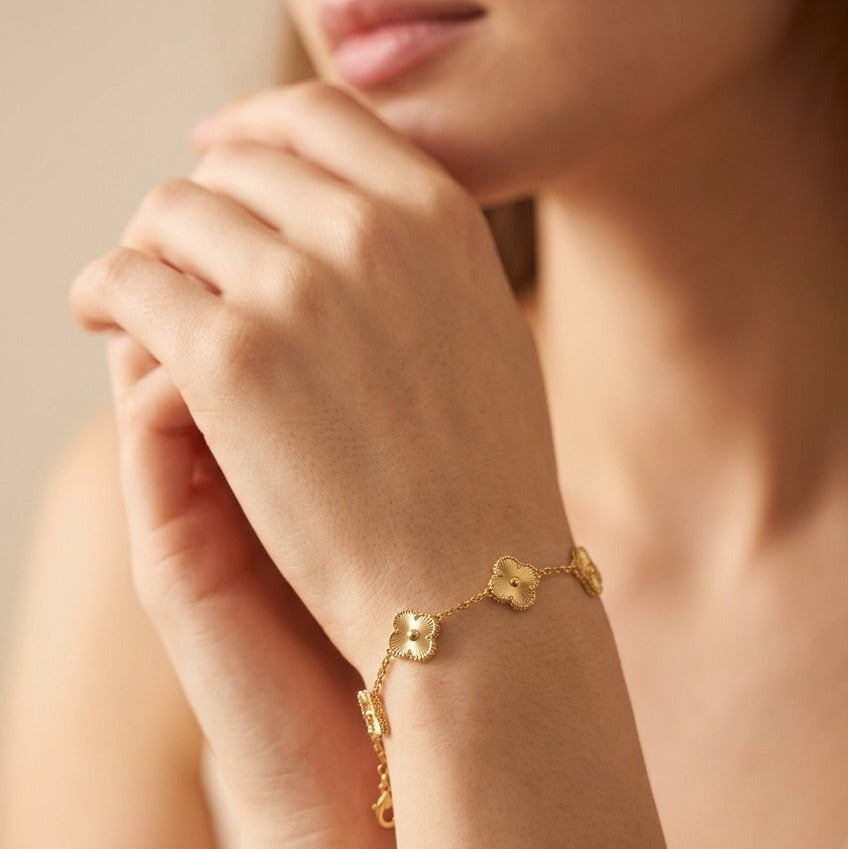 A close-up lifestyle shot of a woman wearing a delicate gold chain bracelet with four connected clover-like charms on her wrist.