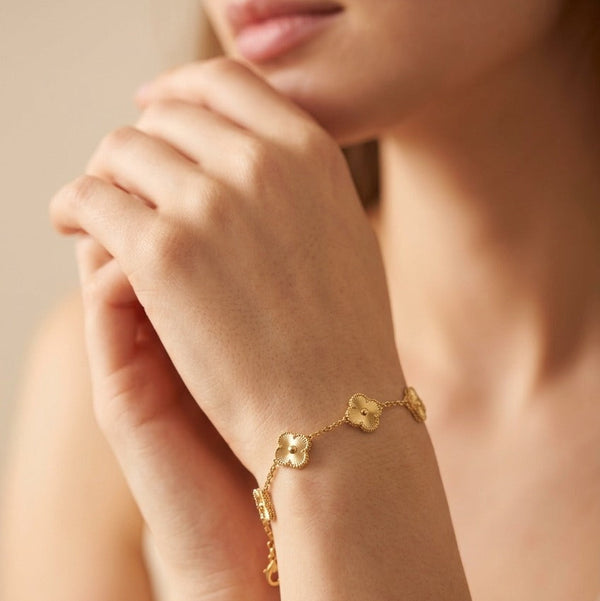 A close-up lifestyle shot of a woman wearing a delicate gold chain bracelet with four connected clover-like charms on her wrist.