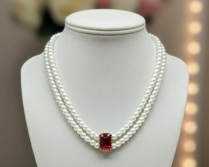 Pearl necklace with a red gemstone on a white mannequin bust against a blurred background