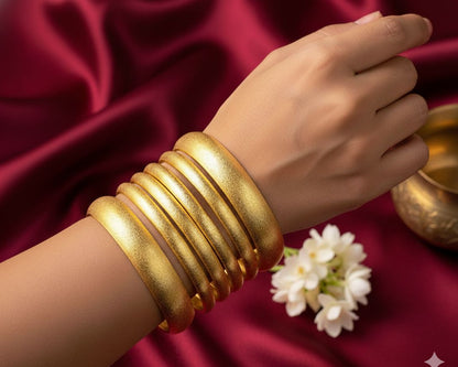 Gold bangles on a hand with a white flower on a red fabric background