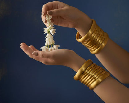 Gold Bangles in hands holding a small bouquet of flowers against a dark background