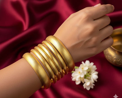 Gold bangles on a hand with a white flower on a red fabric background
