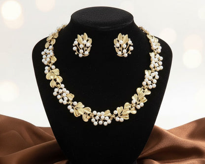 Gold and pearl necklace and earrings set on a black stand with a brown fabric background