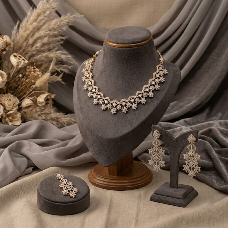 A jewelry set displayed on a gray velvet mannequin bust and stand, including a necklace, matching earrings, and a small round box, styled with draped gray fabric and dried floral decor.