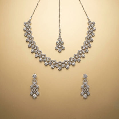 A silver-toned jewelry set featuring a floral choker necklace, a matching pendant, and two matching drop earrings, displayed on a warm beige background.